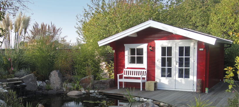 Rotes Gartenhaus aus Holz vor einem Weiher